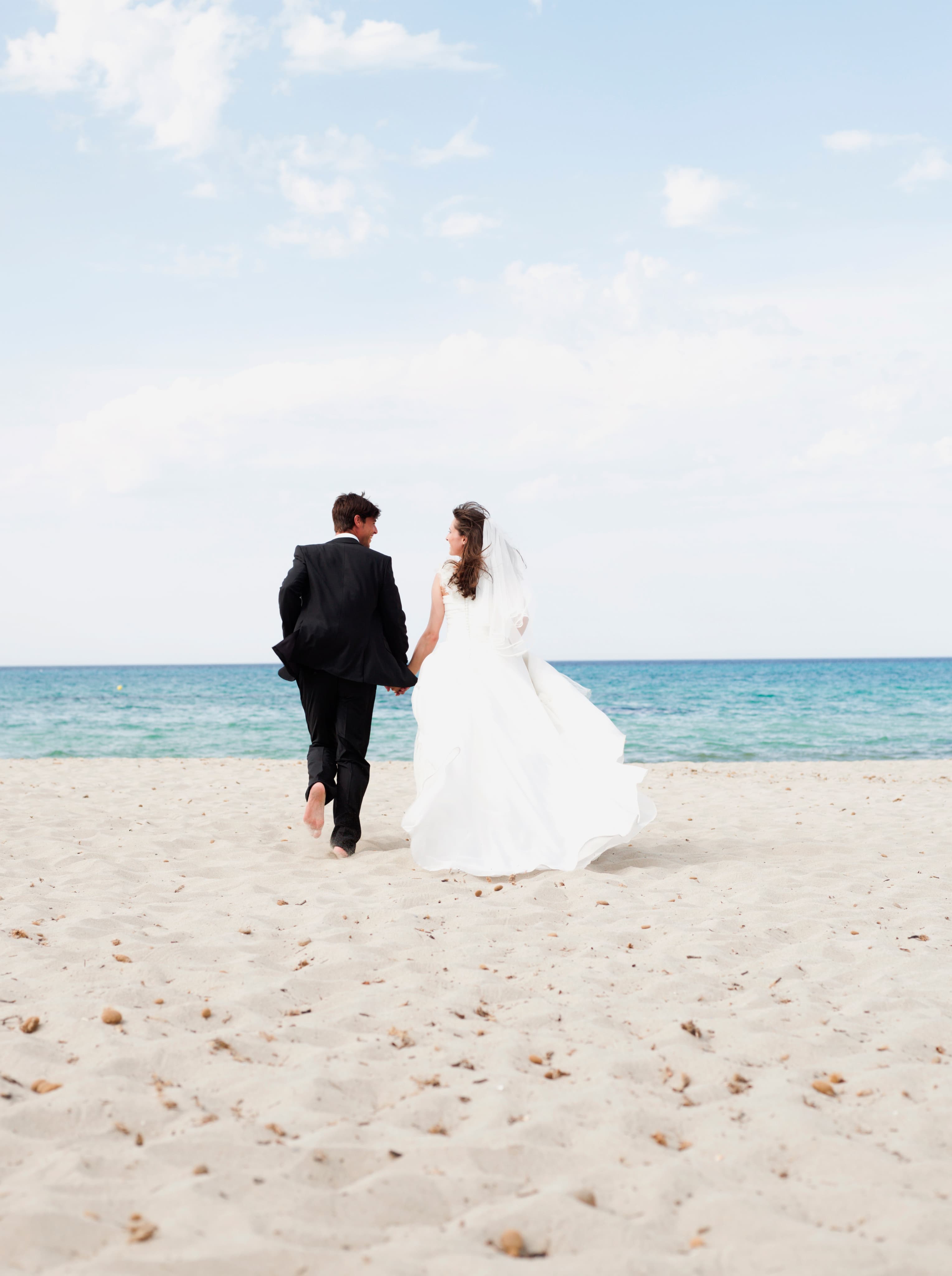 Pareja de recién casados abrazándose bajo un arco de flores en una boda en la playa, con el mar de fondo.